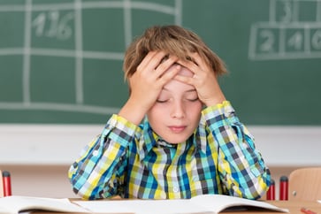 Young boy concentrating on his schoolwork sitting at his desk in the classroom with his head in his hands reading his class notes